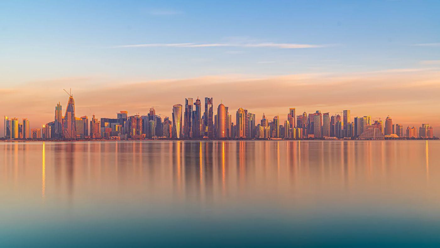 Gulf city skyscrapers reflected in calm water at sunset