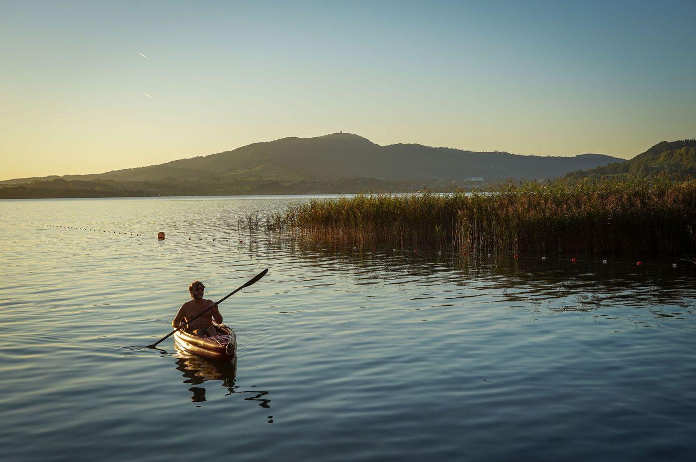 A person kayaking across a calm lake at sunset with mountains behind