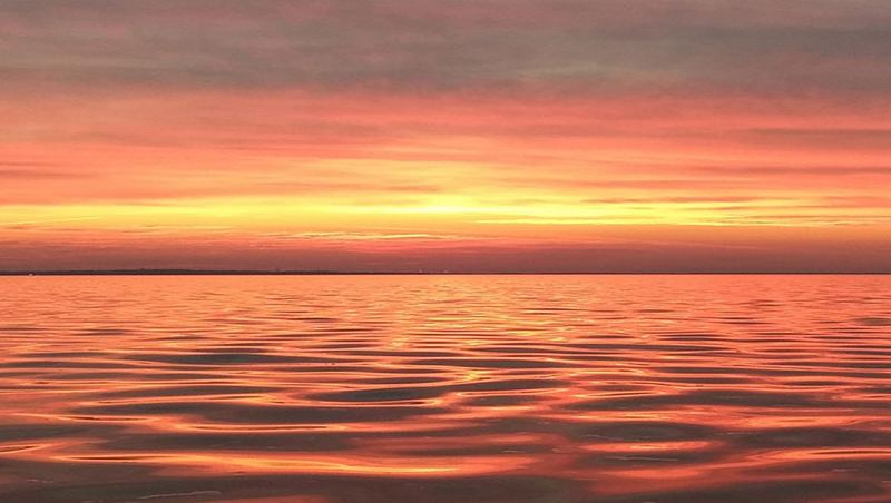 A calm sea under a burnt orange sunset, the light laid flat across the water